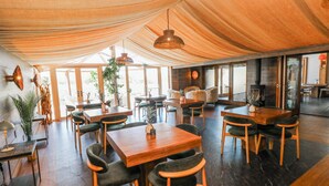 Un vaste espace dédié à la salle à manger, avec des tables et des chaises en bois, de grandes fenêtres et un plafond haut agrémenté de tentures.