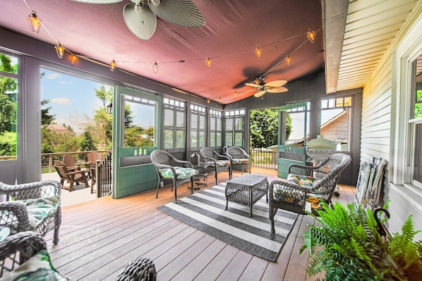 Eine überdachte Terrasse im Freien mit Korbmöbeln, Lichterketten und Deckenventilator.