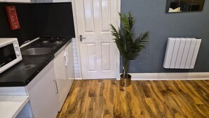 Una cocina con microondas, estufa y lavamanos. Se observa una puerta blanca y una planta en maceta.
