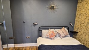 Un dormitorio con una cama, dos almohadones decorativos, una lámpara de pared y un espejo.