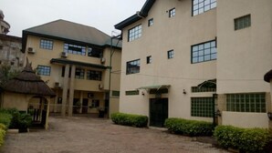 A courtyard with a building featuring multiple windows and a thatched-roof structure. - DAVIES SUITES  (Enugu)