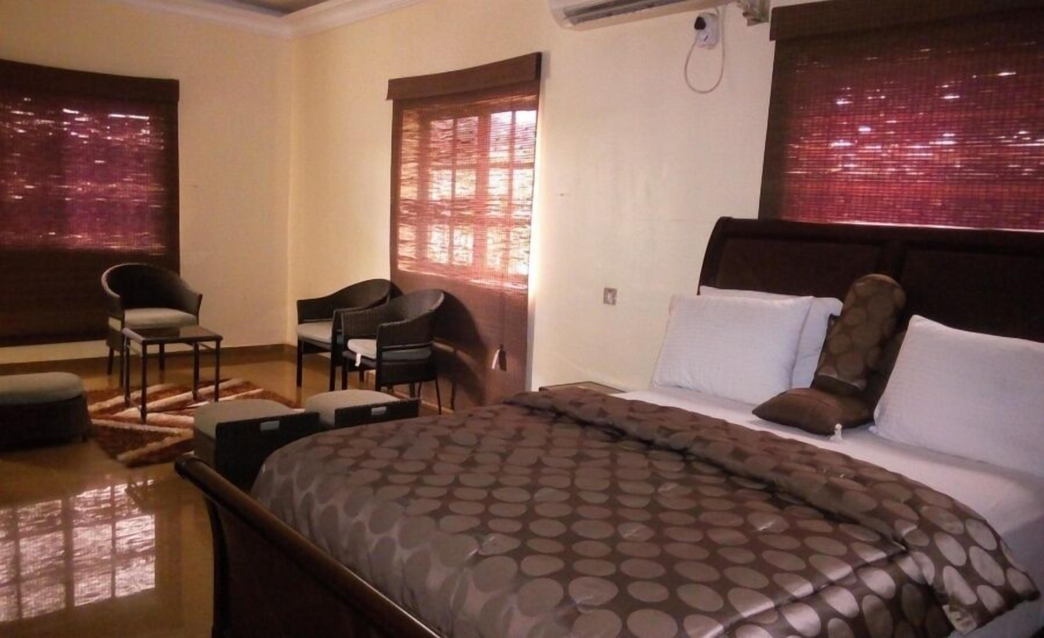 A hotel room with a bed, two chairs, a small table, and a window with blinds.