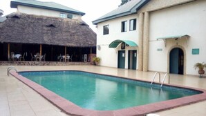 A swimming pool with a thatched-roof structure and a covered seating area. - DAVIES SUITES  (Enugu)