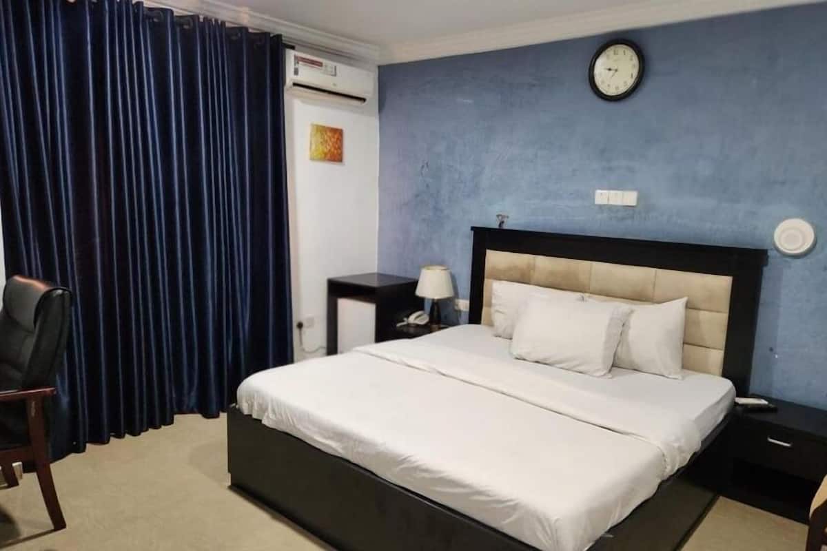 A hotel room with a bed, a nightstand, a lamp, a clock, and a window with curtains.