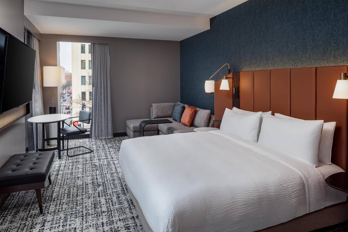 Een hotelkamer met een groot bed, een bank, een tafeltje, een televisie en uitzicht op de stad.