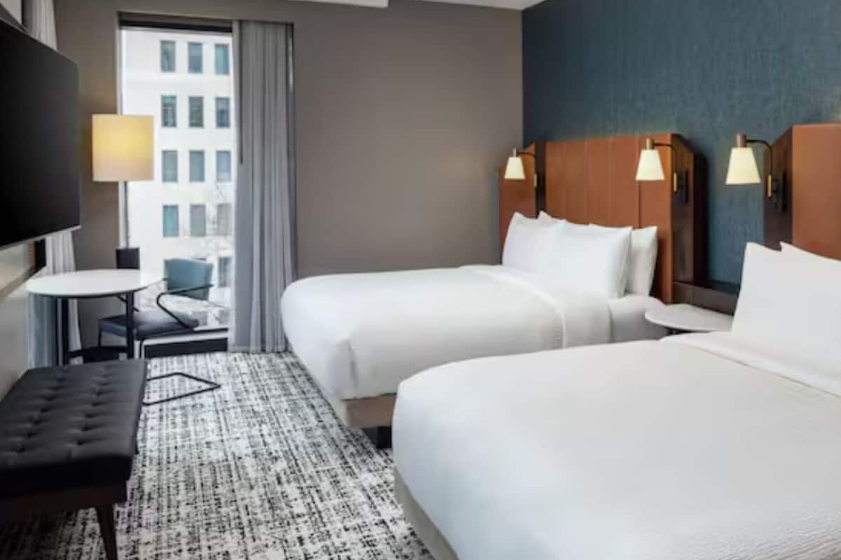 A hotel room with two beds, a desk, a chair, and a TV.