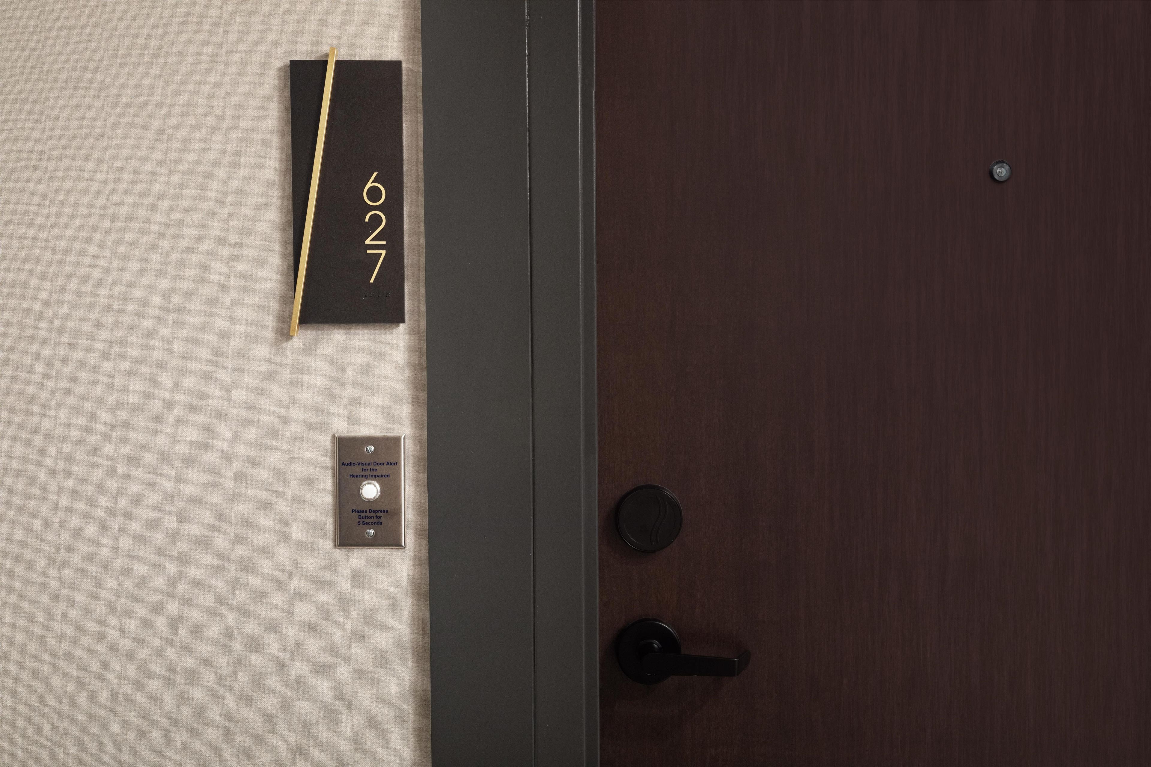 A door with a number plate, a doorbell, and a sign for the hearing impaired.
