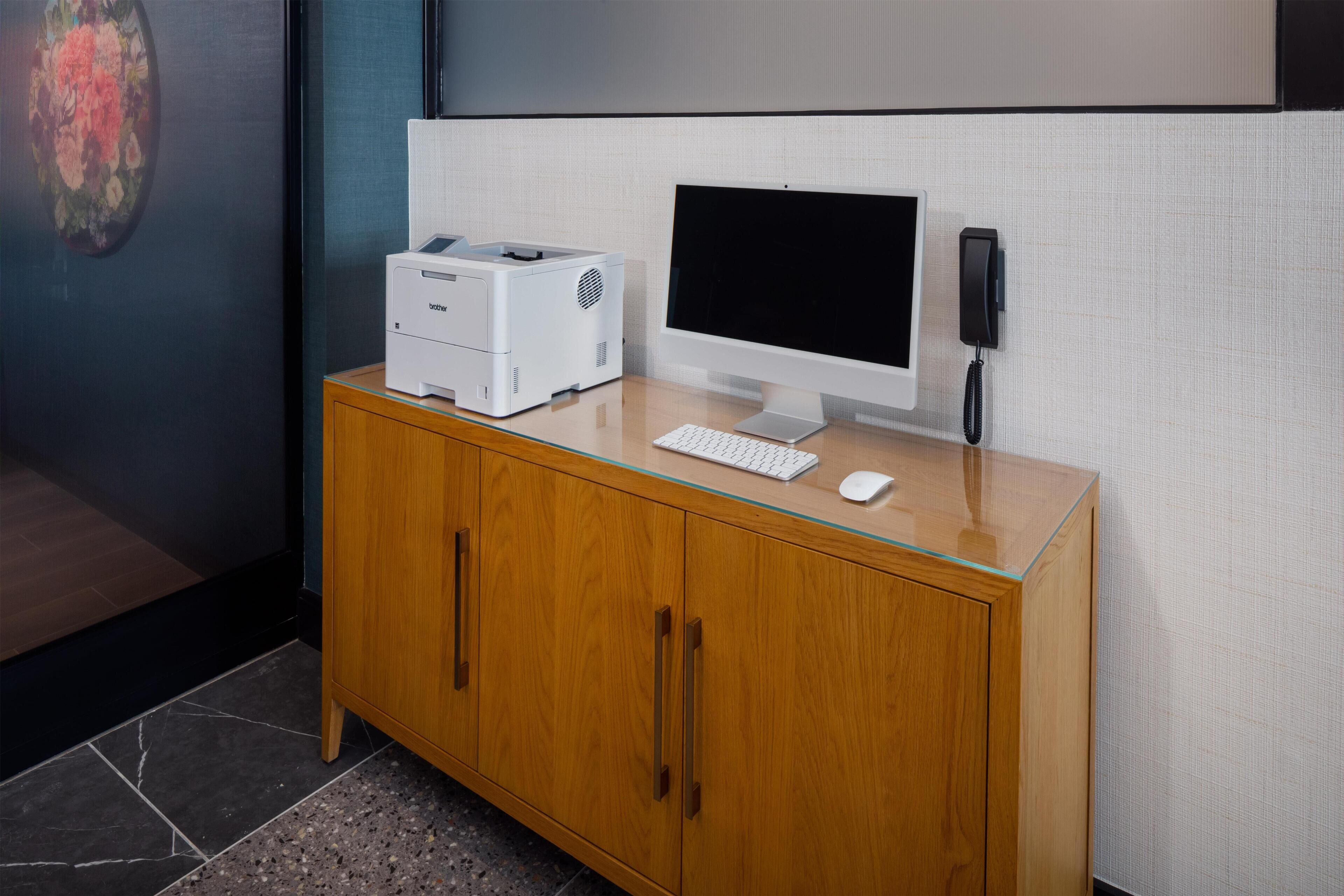 Um computador de mesa em um armário de madeira, com teclado, rato, impressora e telefone.