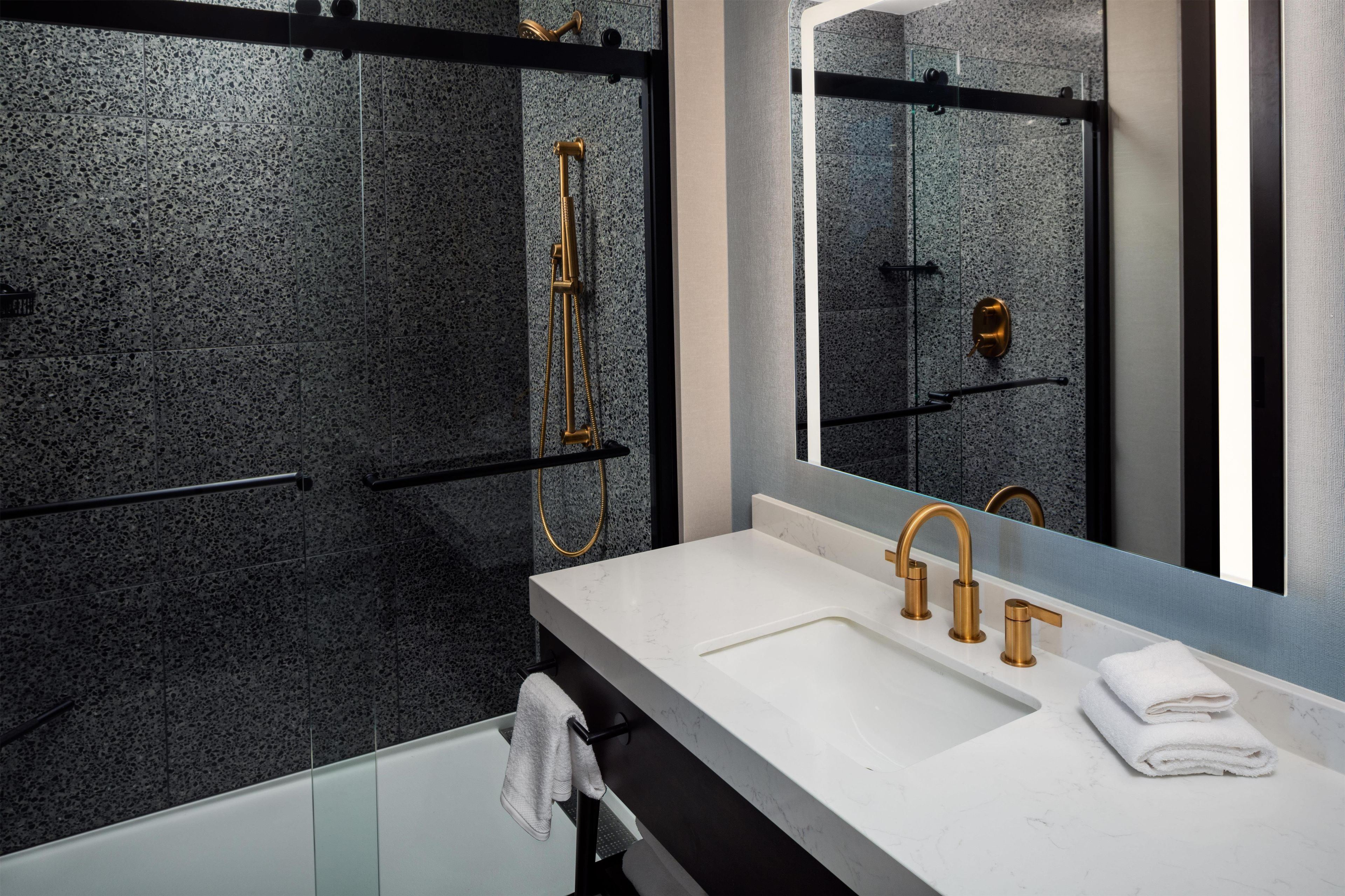 Un baño moderno con lavamanos de mármol blanco, grifería dorada y ducha con cerramiento de vidrio.
