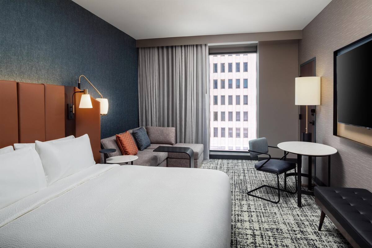 Hotelkamer met een groot bed, een bank, een bijzettafeltje, een stoel, een televisie en een raam met gordijnen.
