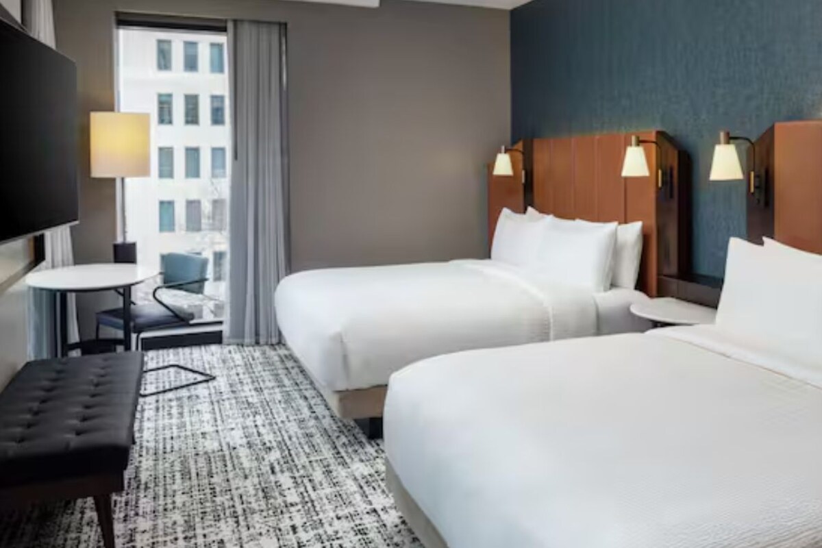 A hotel room with two beds, a desk, a chair, and a TV.