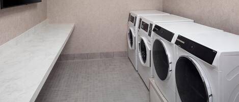 A laundry room with a marble countertop, a flat-screen TV, and three stacked front-loading washing machines.