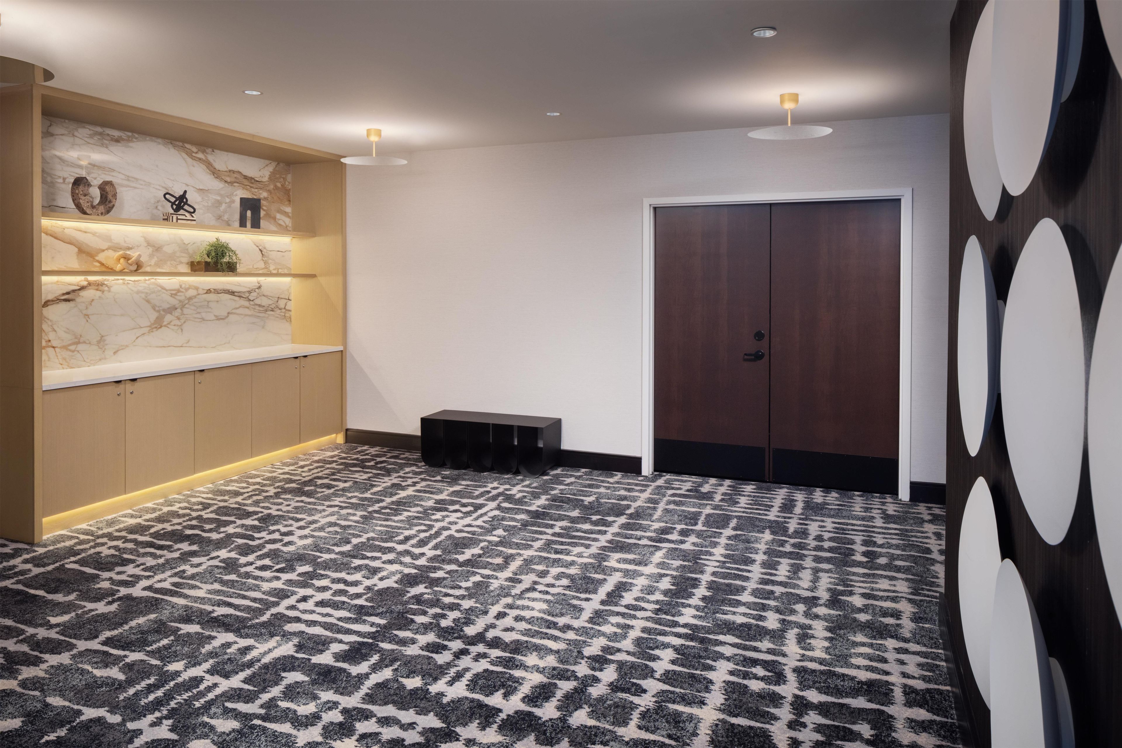 Un vestíbulo de hotel con una pared de mármol, un mostrador de recepción de madera, una alfombra estampada y una puerta de madera oscura.