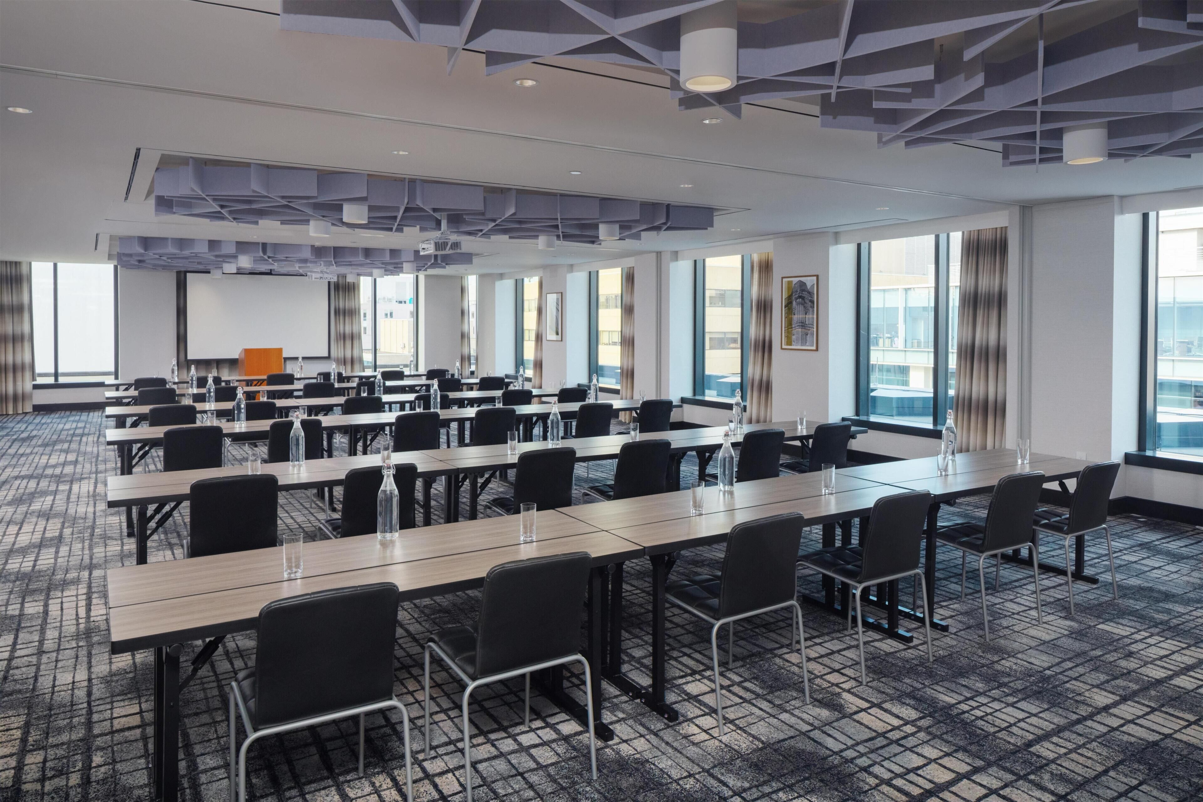 Un salón de conferencias con varias mesas y sillas, ventanas amplias y un diseño de techo moderno.