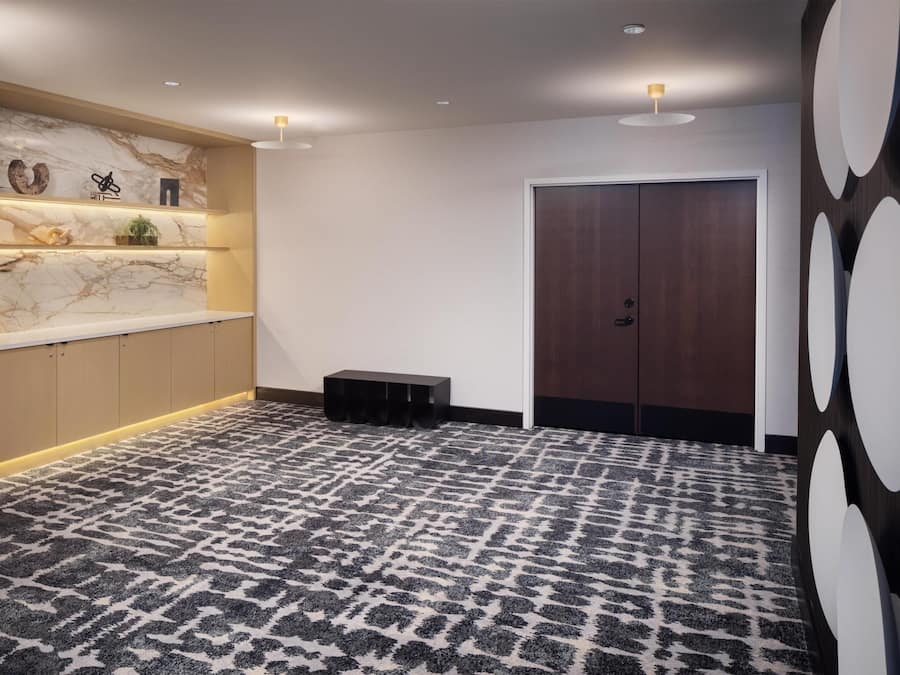 Een hotel lobby met een marmeren wand, houten kasten, een kamerbreed tapijt met dessin, een deur en een wand met cirkelvormige decoraties.