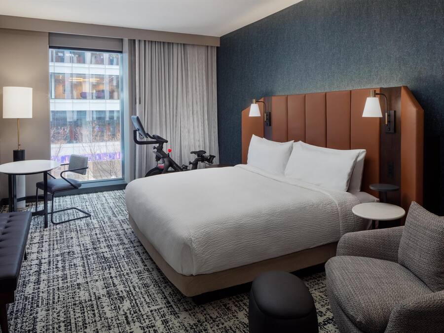 A hotel room with a large bed, a seating area with a chair and ottoman, a small table, and a TV.
