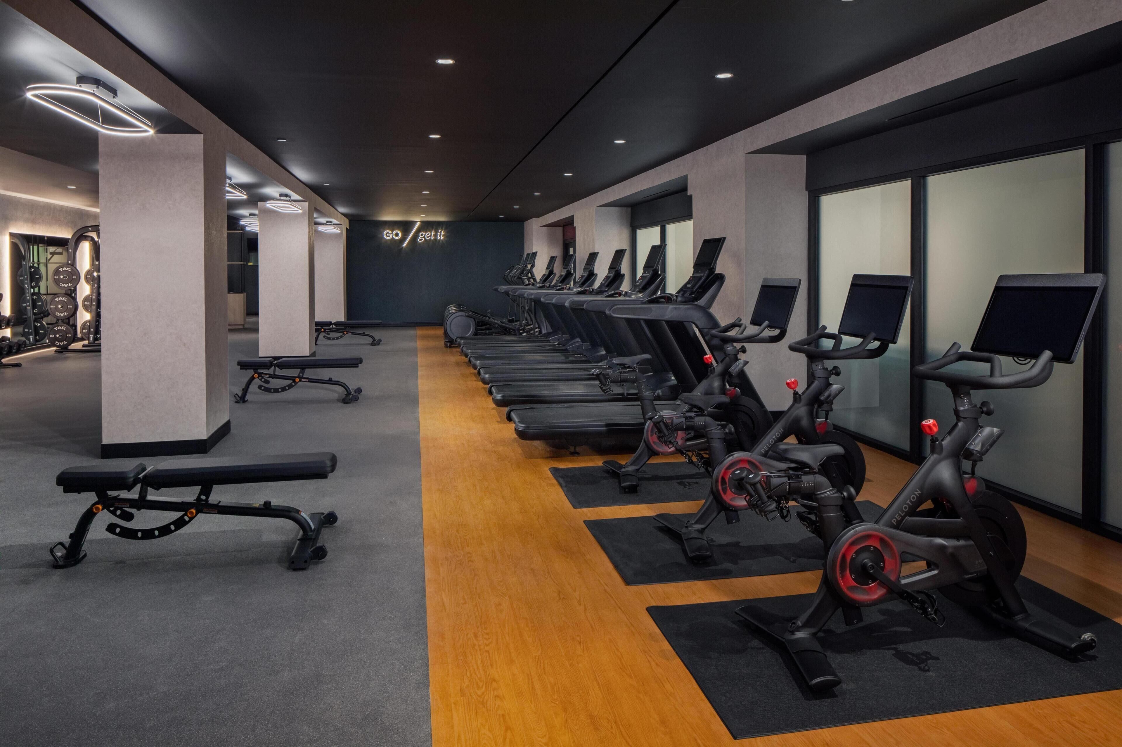 Un gimnasio con cintas de correr, bicicletas estáticas y bancos.