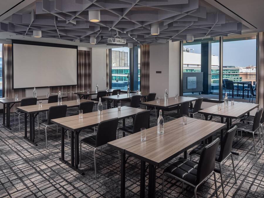 Sala de conferências com tela grande, várias mesas, cadeiras e vista para a cidade.