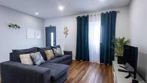 Ein modernes Wohnzimmer mit einem grauen Sofa, einem Flachbildfernseher und einem Holzboden.