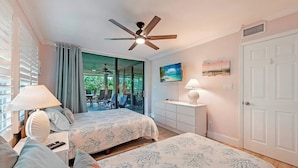 A bedroom with two beds, a ceiling fan, a TV, and a view of the outdoors. - Wild Pines A307 (Bonita Springs)