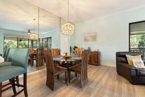 A modern living room with a glass dining table, wooden chairs, a leather sofa, and a large window offering a view of greenery. - Wild Pines A307 (Bonita Springs)