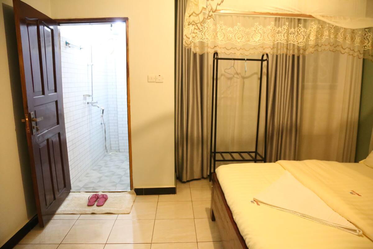A hotel room with a bed, a wooden door, a bathroom with a shower, and a curtain.