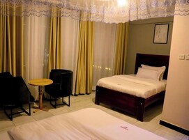 Una habitación de hotel con cama, una silla, una mesita y cortinas.