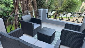 Eine Terrassengruppe im Freien mit Korbmöbeln, darunter Sofas und ein Couchtisch, umgeben von einem Metallgeländer.