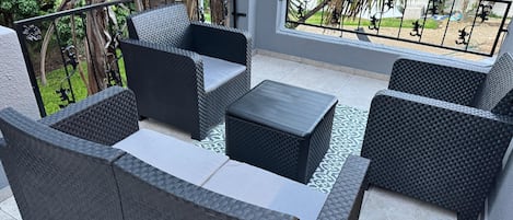 Une terrasse extérieure aménagée avec des meubles en osier, notamment des canapés et une table basse, le tout entouré d’une rambarde en métal.