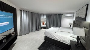Ein modernes Hotelzimmer mit einem großen Bett, einem Fernseher links und einem Schreibtisch mit einer Lampe.