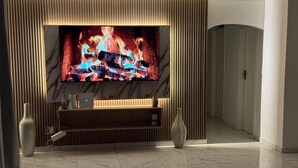 Ein modernes Wohnzimmer mit großem Flachbildfernseher an einer Holzwand, Marmorboden und minimalistischem Design.