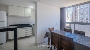 A modern kitchen with white cabinets and a black countertop, a dining area with a table and chairs, and a large window offering a city view. - Apartments Just 270 Meters From Praia do Morro, Guarapari - Epus (Guarapari)
