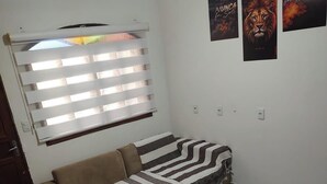 Une pièce avec un canapé, une fenêtre avec des stores et trois affiches au mur.