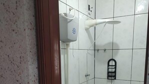 Une petite salle de bain carrelée, équipée de toilettes, d’une douche et d’un sèche-mains.