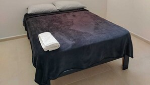 A single bed with a dark cover, two pillows, and a folded white towel. - Hotel Morelia Nova (Morelia)