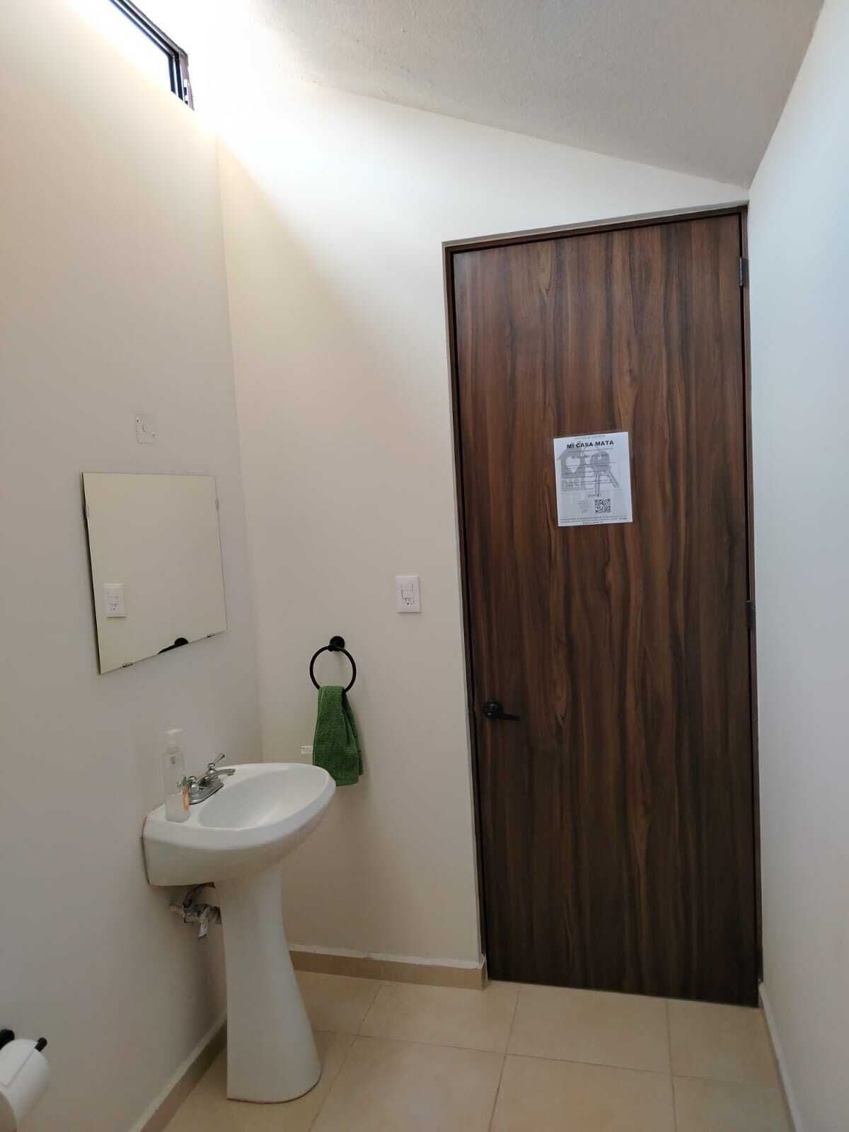 A bathroom with a white sink, a mirror, a towel ring with a green towel, and a wooden door with a sign.