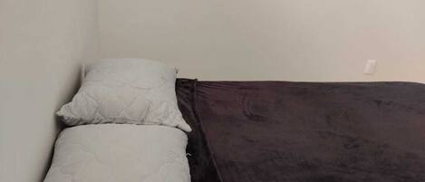 A small, single-bed room with a dark-colored bedspread and a white pillow.