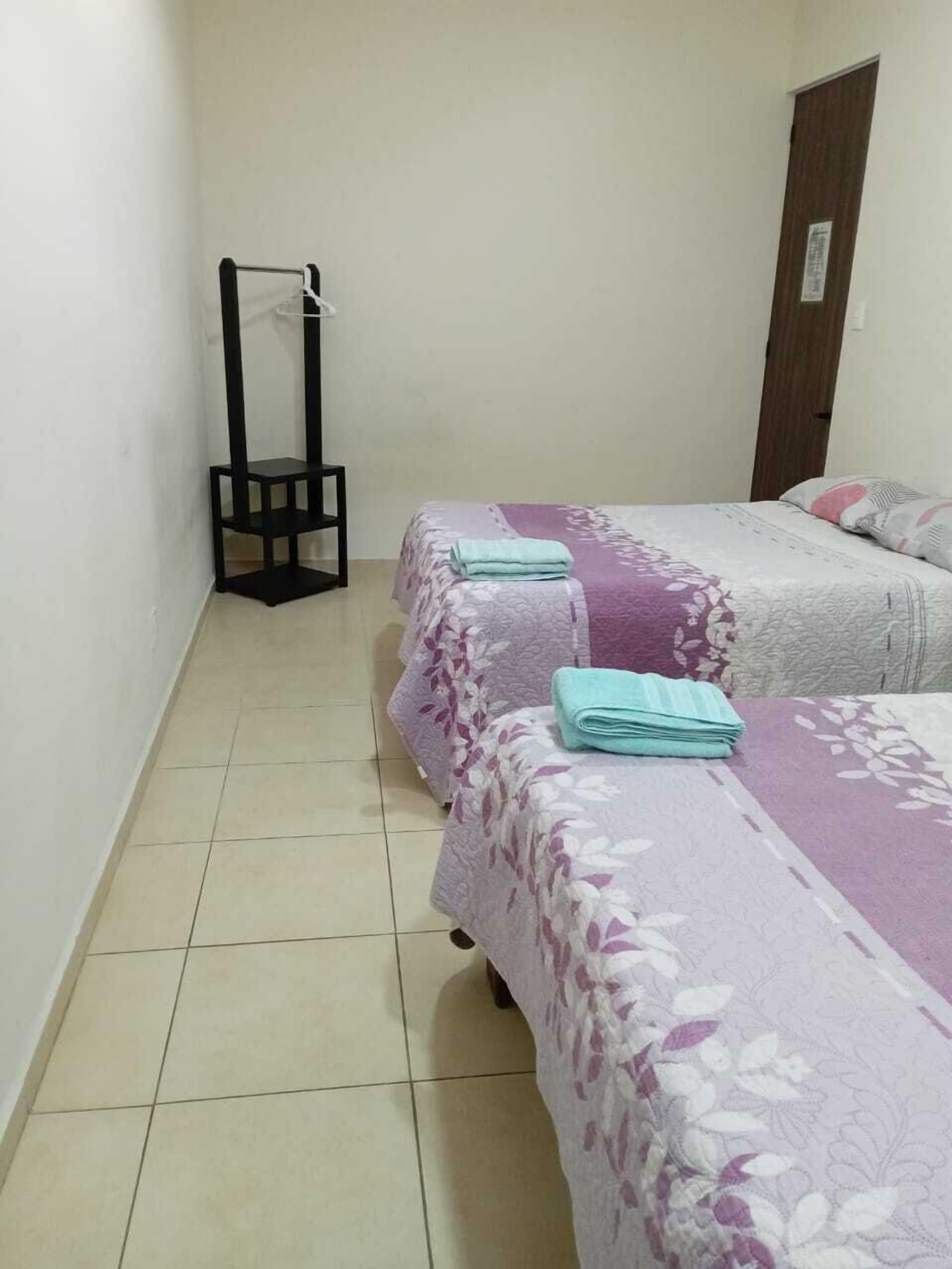 A small, clean room with two beds, a wooden wardrobe, and a black chair.