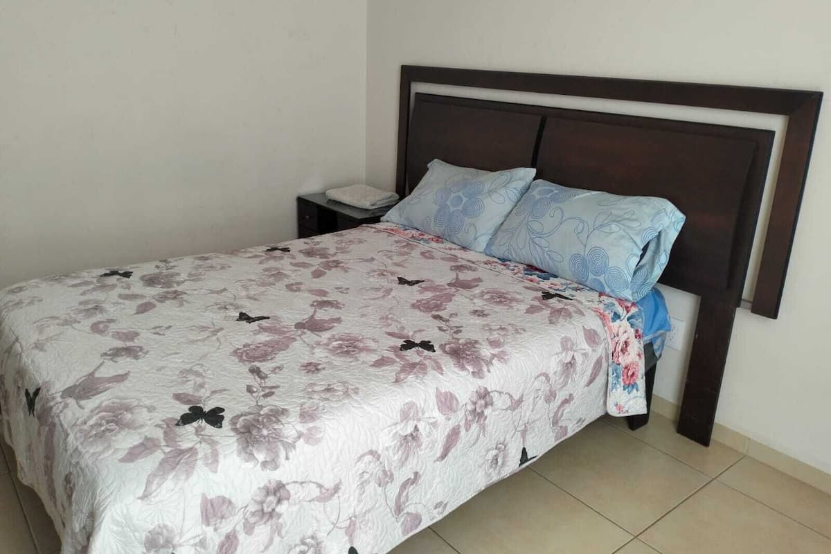 A bed with a floral bedspread, a wooden headboard, and a nightstand with a lamp.