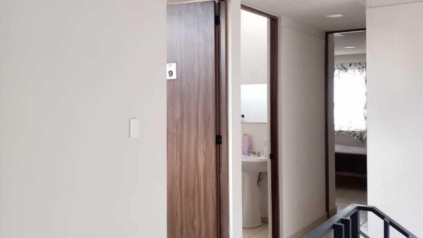 A hallway with a wooden door marked '9', a bathroom with a sink, and a staircase with a black railing. - Hotel Morelia Nova (Morelia)