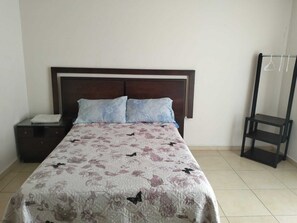 A bedroom with a bed, a nightstand, a wooden headboard, and a black metal shelf unit. - Hotel Morelia Nova (Morelia)