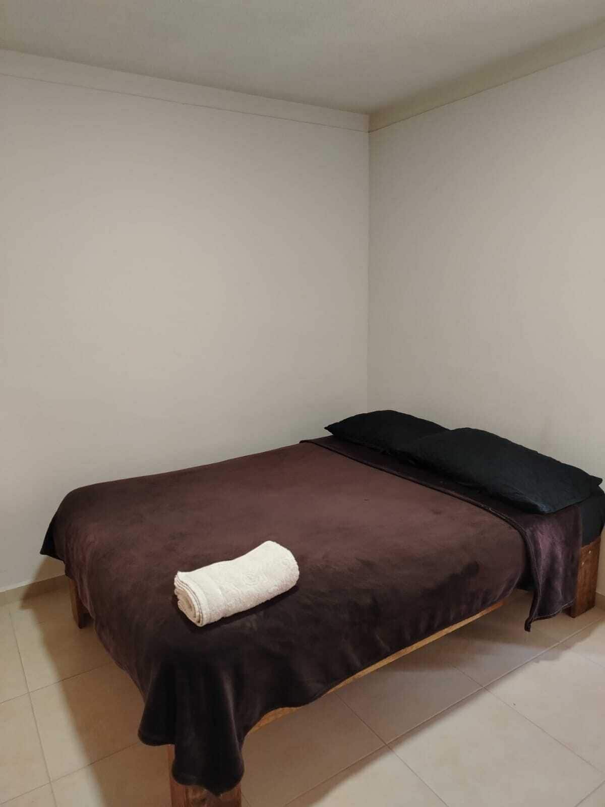 Una cama individual con una colcha marrón y una toalla blanca.