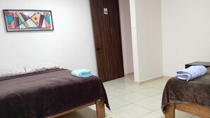 A room with two wooden beds, each with a dark blanket and a folded towel on top. A colorful abstract painting hangs on the wall above the beds. - Hotel Morelia Nova (Morelia)