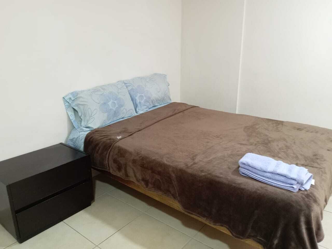 A small, single-bed room with a brown bedspread, a blue pillow, and a black nightstand.