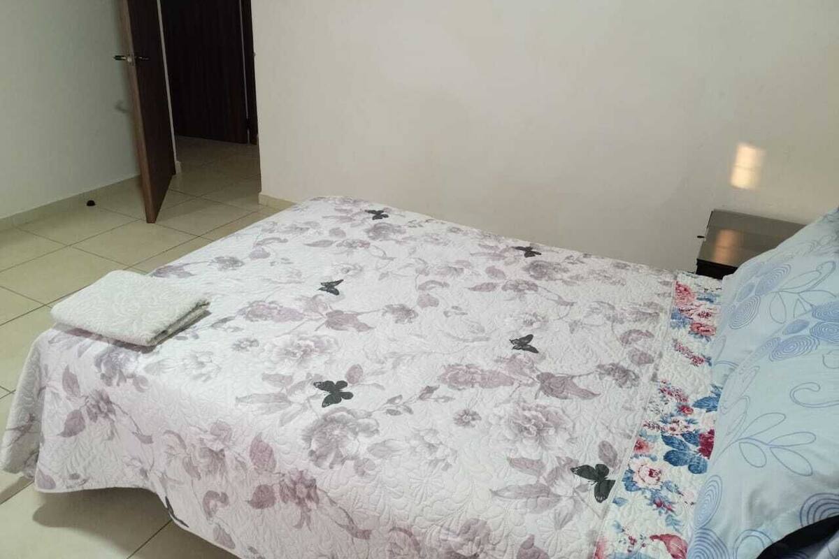 A bedroom with a bed covered in a floral bedspread, a white pillow, and a nightstand with a lamp.