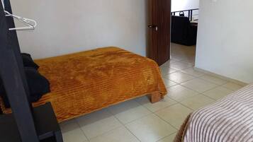 Ein kleines Zimmer mit einem Einzelbett, Holzboden, einer Tür zu einem anderen Raum und einem Bett mit einer gestreiften Decke.