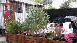 Un jardín con bancales de madera, sillas blancas y una maceta colgante.