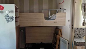 Una habitación compacta con una cama de madera integrada, un refrigerador blanco con calcomanías decorativas y una ventana pequeña.
