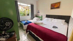 Habitación de hotel con dos camas, un ventilador, una ventana con cortinas y un cuadro en la pared.