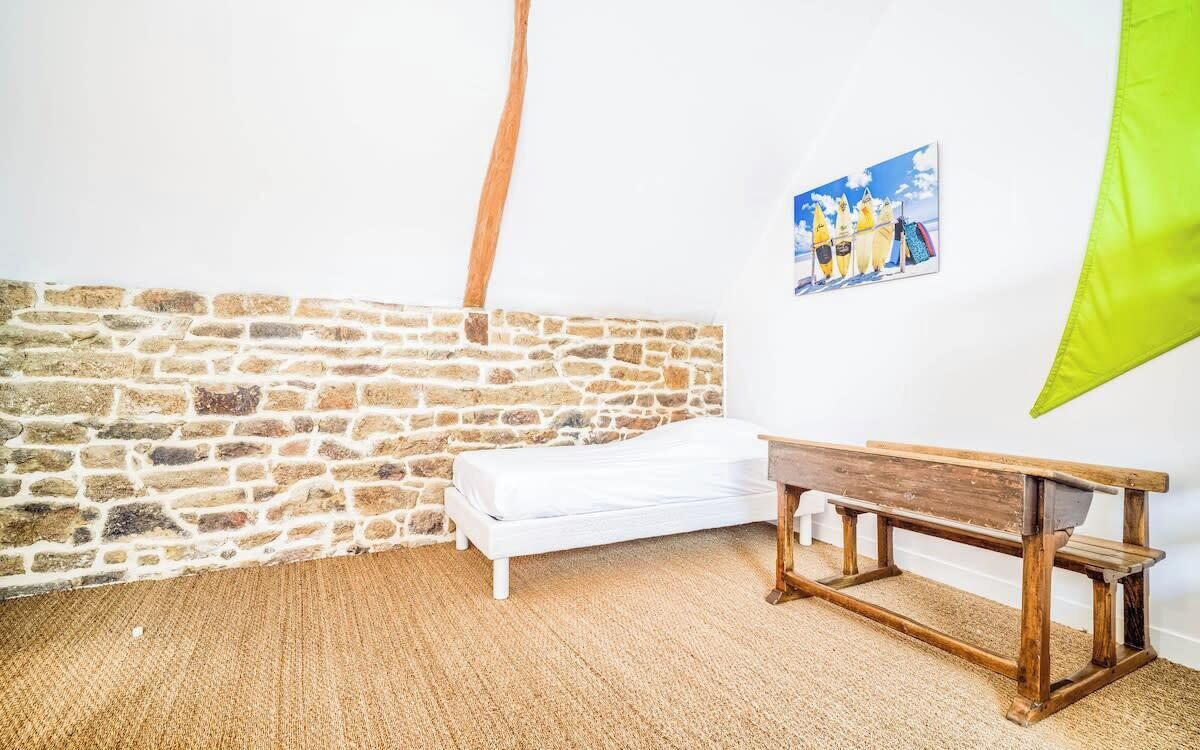 Una habitación con pared de piedra, un banco blanco, una cama pequeña y un cuadro en la pared.